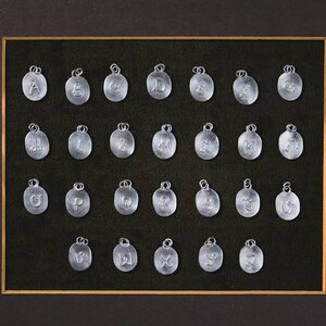 May include: A framed display of 26 silver charms, each featuring a different letter of the alphabet. The charms are arranged in rows and columns on a black velvet background.