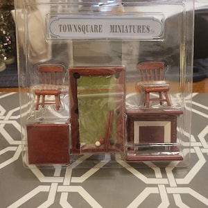May include: Miniature TownsSquare billiards room set in a clear plastic package. The set includes a pool table with a green felt surface, two chairs, a bar, and a small side table. The set is made of wood and has a dark brown finish.