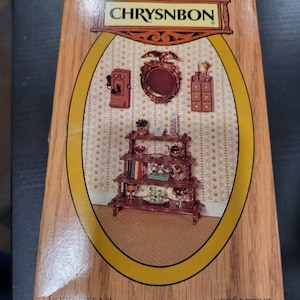 May include: A box for a miniature dollhouse furniture set by Chrysnbon. The box shows a brown wooden shelf unit with a mirror, a phone, and other decorative items. The box is labeled "Model F-130" and "See Back Panel for Contents".