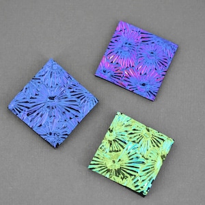 May include: Three iridescent glass tiles with a floral pattern. The tiles are square and have a blue, purple, and green color scheme.