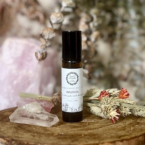 May include: A dark amber glass aromatherapy roll-on bottle with a black cap and a white label. The label features a circular logo, the text 'AROMATHERAPY ROLL-ON', 'INTUITION', 'tune into your inner knowing', and '1/3 OZ | 10ML' with floral line art.