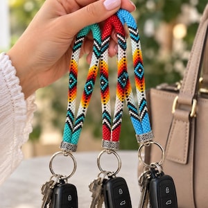 May include: Three beaded keychains featuring intricate geometric patterns in turquoise, red, and blue, accented with white and yellow. Each strap is finished with a silver-toned metal bead cap and a circular split ring holding metal keys and a black fob.