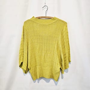 May include: A yellow knitted sweater with a ribbed texture and a round neckline. The sweater has a relaxed fit and short sleeves.