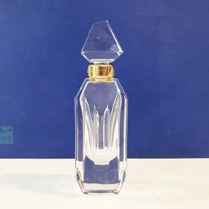 May include: A clear glass bottle with a gold top and a faceted design. The bottle is empty and has a diamond-shaped stopper.