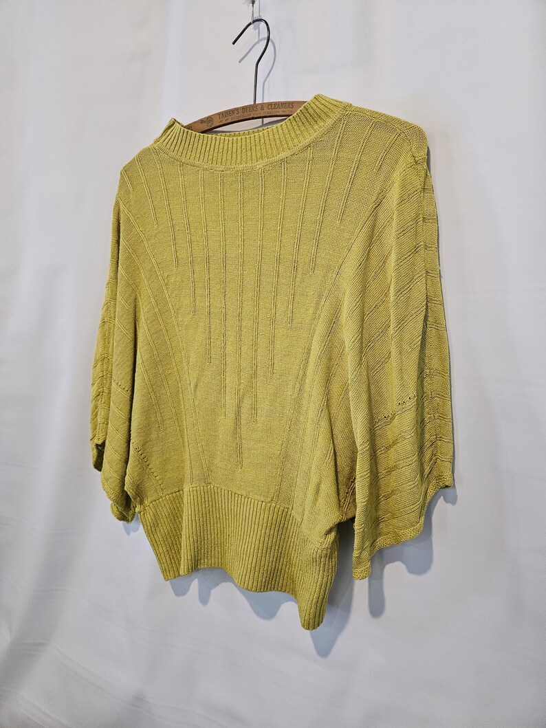 May include: A yellow knitted sweater with a round neckline and short sleeves. The sweater has a ribbed texture and a slightly cropped length.