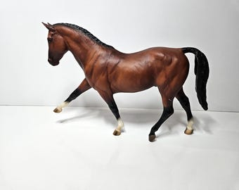 May include: A brown horse figurine with a black mane and tail, and black legs with white markings. The horse is posed with one leg raised, suggesting movement. The figurine is set against a white background.