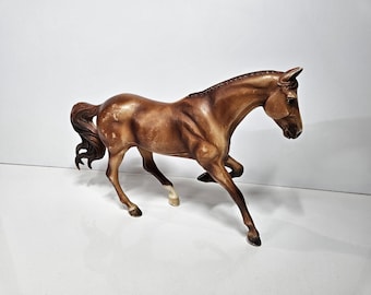 May include: A brown horse figurine in a running pose. The horse has a detailed mane and tail, with white markings on its legs. The figurine is made of a glossy material and is set against a white background.