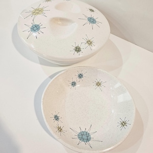 May include: A white ceramic serving dish and bowl with a speckled finish. The dish has a lid with three compartments and a handle. Both pieces are decorated with blue and yellow starburst designs.