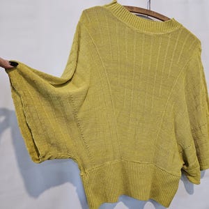May include: A yellow knitted sweater with a round neckline and short sleeves. The sweater has a ribbed texture and a slightly loose fit.