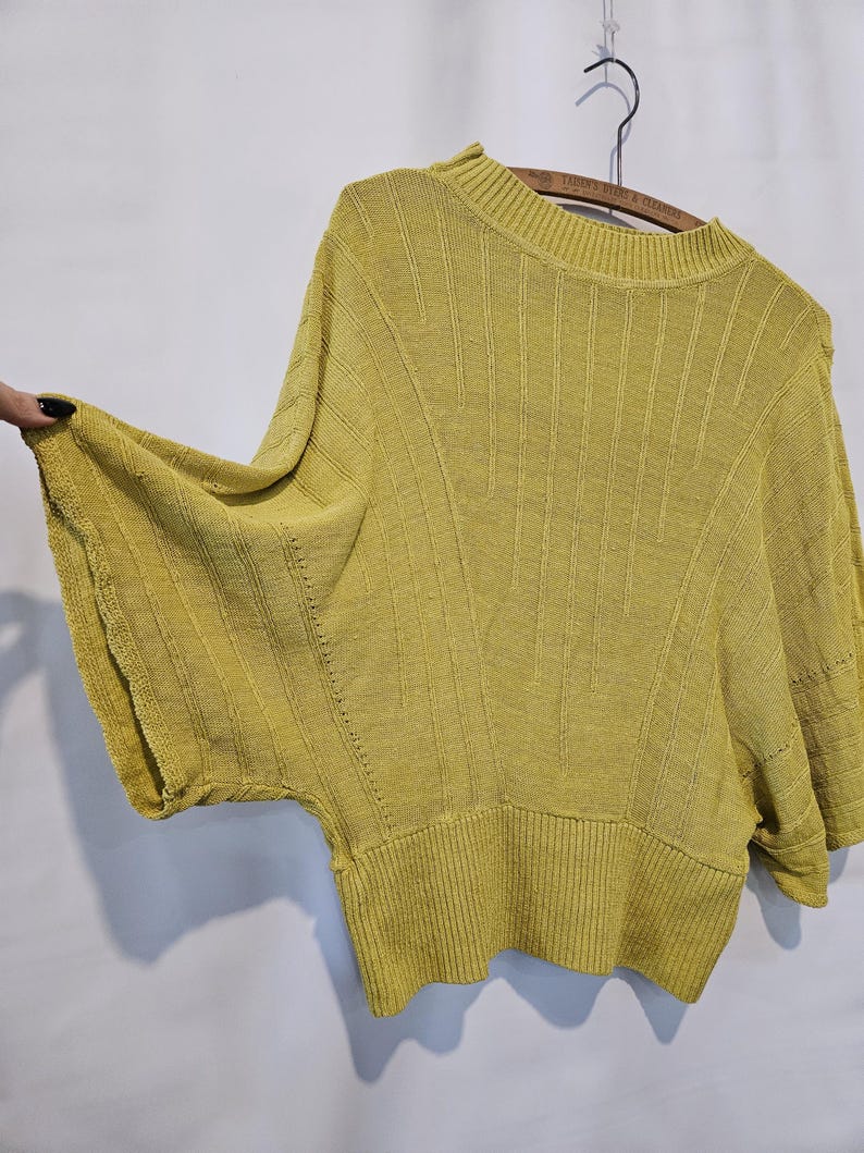 May include: A yellow knitted sweater with a round neckline and short sleeves. The sweater has a ribbed texture and a slightly loose fit.