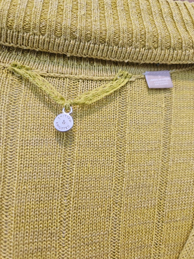 May include: A close-up of a yellow knitted sweater with a small silver tag that says "Knitted & Knotted".