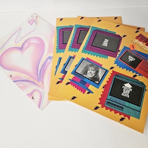 May include: A collection of vintage photo albums and a binder. The binder features a pink heart design. The photo albums have a yellow background with retro computer graphics and the text "YOU GOT THAT LOOK".