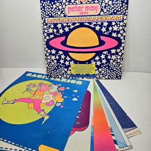 以下が含まれることがあります： 1971年のピーター・マックスのヴィンテージ占星術カレンダー。カラフルなイラストが特徴です。表紙は、白い星が散りばめられた青い背景に、ピンクのリングが付いた惑星のデザインです。いくつかの占星術チャートが扇状に広がっています。