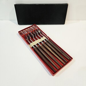 Puede incluir: Juego de seis tenedores de plata con mangos de madera en una caja roja. Los tenedores están dispuestos en fila, con los mangos apuntando hacia la derecha. La caja está abierta y los tenedores son visibles.