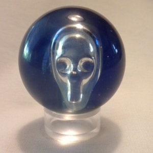 May include: A blue glass marble with a clear, raised design of an alien face.