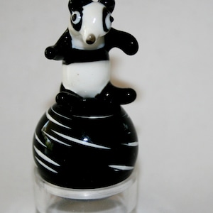 May include: A black and white glass panda figurine standing on a black and white striped ball. The figurine is sitting on a clear glass base.