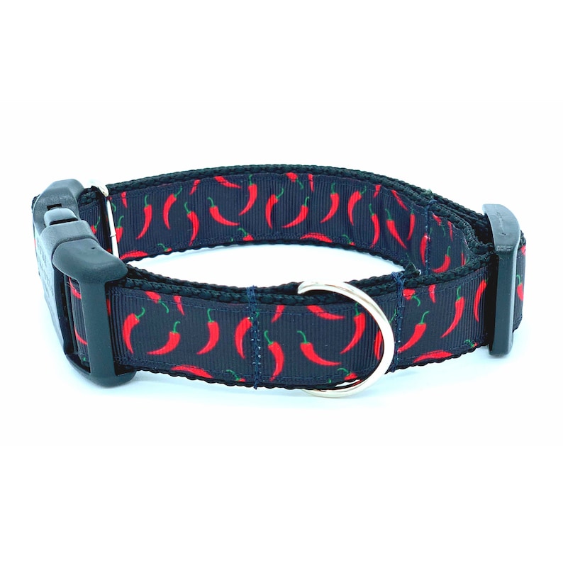 May include: A black dog collar with a red chili pepper pattern. The collar has a black buckle and a silver D-ring.