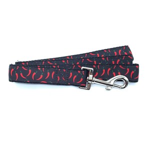 May include: A black dog leash with a red chili pepper pattern. The leash has a silver clip.