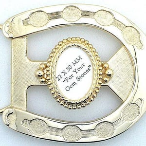 May include: A gold-colored metal belt buckle in a horseshoe shape. The buckle has an oval-shaped inset with the text "22 X 30 MM For Your Gem Stones". The buckle has a textured design with decorative circular accents.
