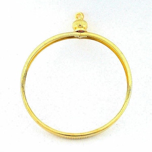 May include: A gold-colored pendant frame with a circular design. The frame has a small, decorative top with a loop for hanging. The pendant is made of a shiny, metallic material.