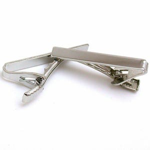 May include: Two silver-colored tie clips are displayed against a white background. The clips have a rectangular bar and a hinged clip mechanism. The metal has a shiny, reflective surface, suggesting a polished finish. These accessories are designed to secure a necktie.