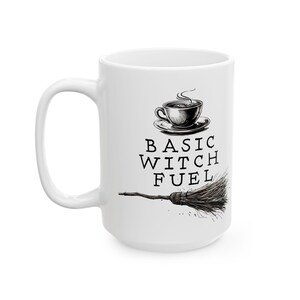 May include: White ceramic mug with the words "BASIC WITCH FUEL" in black, along with a drawing of a coffee cup and a broom. The mug has a large handle and is designed for hot beverages.