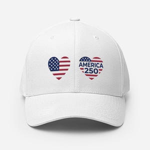 Könnte beinhalten: Eine weiße Baseballkappe mit zwei herzförmigen Grafiken auf der Vorderseite. Das linke Herz zeigt die Sterne und Streifen der amerikanischen Flagge, während das rechte Herz den Text AMERICA 250 in blauen Buchstaben auf rot-weißen Streifen enthält.