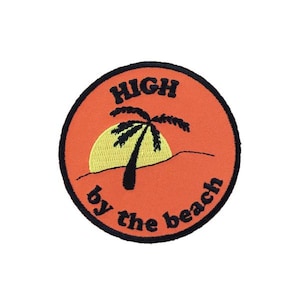 May include: A round orange patch with black stitching. The patch features a palm tree silhouette with a yellow sun behind it. The text "HIGH by the beach" is written in black around the palm tree.