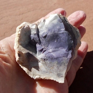 May include: A close-up of a purple and white opal rock. The rock is rough and has a natural, irregular shape.