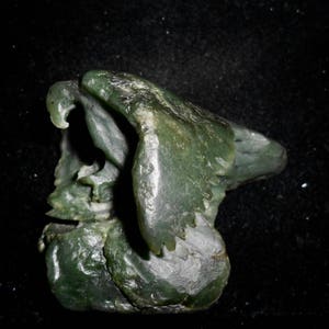 May include: A green jade carving of a bird's head, with intricate details and a textured surface.