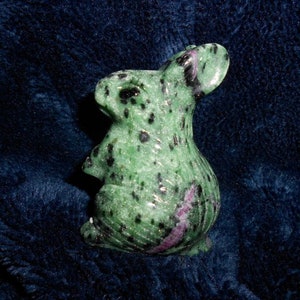 May include: A green and black rabbit figurine carved from green aventurine gemstone. The rabbit has a pink stripe on its back.