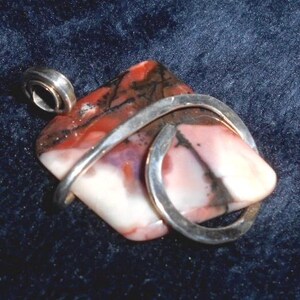 May include: A silver pendant with a pink, white, and black agate stone wrapped in a silver wire.