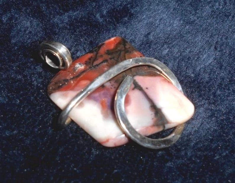 May include: A silver pendant with a pink, white, and black agate stone wrapped in a silver wire.