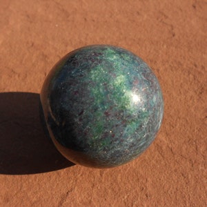 Könnte beinhalten: Eine dunkelgrüne und schwarze Kugel mit einem gesprenkelten Muster. Die Kugel ist aus poliertem Stein und hat eine glatte, glänzende Oberfläche.