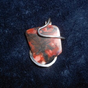 May include: A pendant featuring a red, pink, and black stone with a silver wire wrap.
