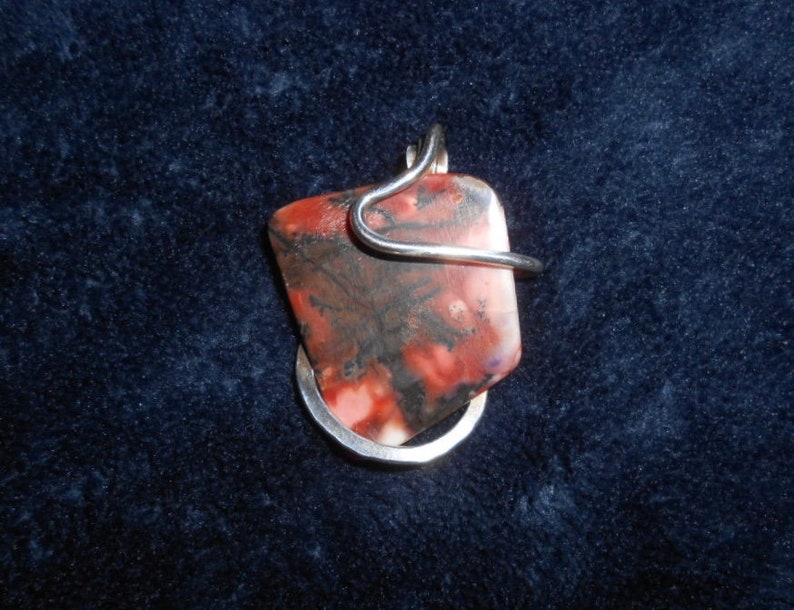 May include: A pendant featuring a red, pink, and black stone with a silver wire wrap.