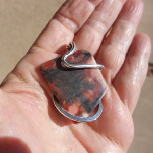 May include: A silver wire wrapped pendant featuring a rectangular, red, white, and black stone.