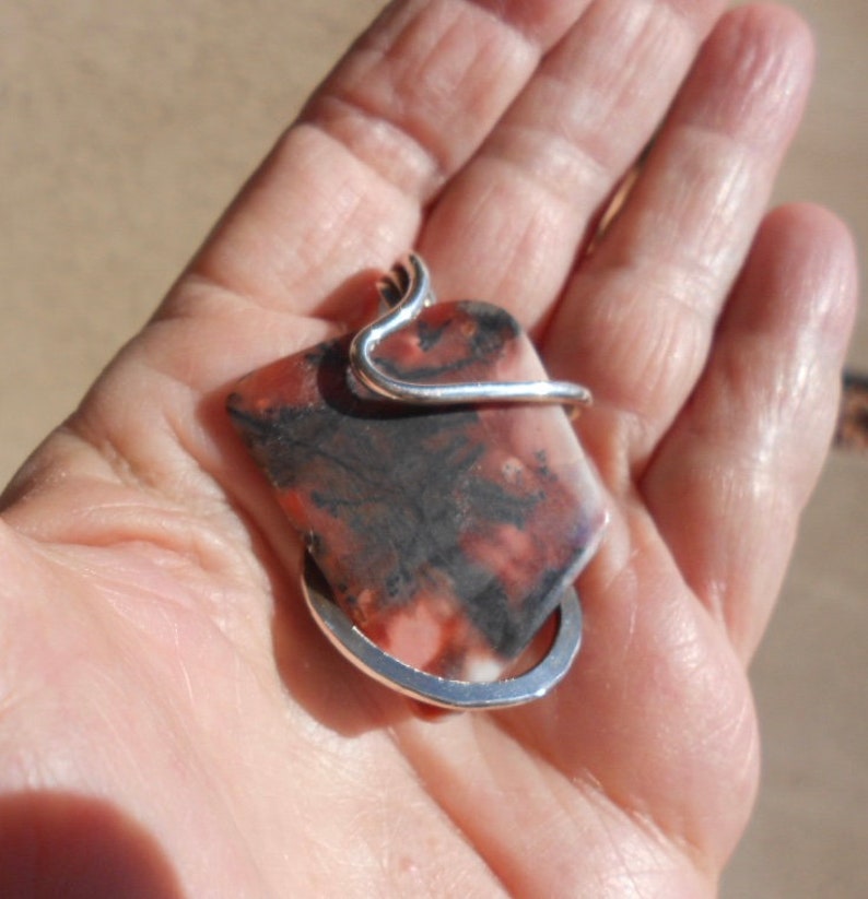 May include: A silver wire wrapped pendant featuring a rectangular, red, white, and black stone.