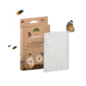 Può includere: Un tappeto di semi per fiori, con il testo "Aktion Bienenwohl" e "Nektarreicher Blütenteppich". Il tappeto è bianco con piccoli semi visibili, e la confezione è marrone con illustrazioni di api e farfalle. Una farfalla è appoggiata sul tappeto.