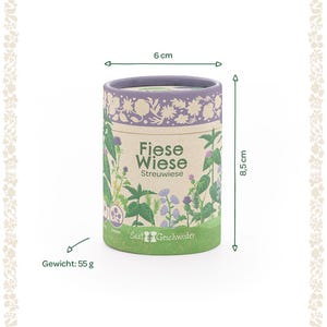 Puede incluir: Un recipiente cil&iacute;ndrico de 6 cm de di&aacute;metro y 8,5 cm de alto, con el texto "Fiese Wiese Streuwiese" e ilustraciones de plantas. El recipiente es verde en la base, beige en el medio y morado en la parte superior. Pesa 55 g.