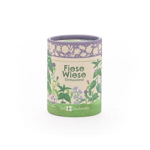 Puede incluir: Un recipiente cil&iacute;ndrico con un dise&ntilde;o floral y bot&aacute;nico. El recipiente tiene un borde y una base de color p&uacute;rpura claro, con las palabras "Fiese Wiese" y "Streuwiese" impresas en la parte delantera. El recipiente est&aacute; lleno de semillas.