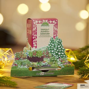 Può includere: Un calendario dell'Avvento rosso e bianco con la scritta "Saatgut-Adventskalender" e una scena di giardino. Il calendario presenta un design pop-up con un giardino in miniatura e un albero di Natale. La parte inferiore del calendario riporta la scritta "Saat Geschwister".