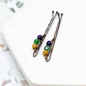 May include: Two gold, green and purple beaded hair clips. The clips are made of wire and have a simple design.