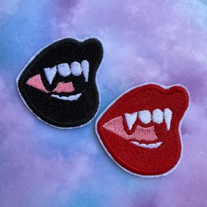 May include: Two embroidered iron-on patches featuring a set of fangs and lips. One patch is black with pink and white fangs, and the other is red with pink and white fangs.