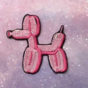 May include: Pink embroidered iron-on patch of a balloon animal shaped like a dog.