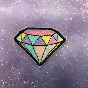 May include: A colorful embroidered diamond-shaped patch with a black outline. The diamond is filled with pink, yellow, blue, and purple embroidery.