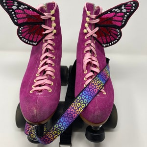 May include: Purple roller skates with pink laces and butterfly appliques. The skates have a rainbow leopard print strap.