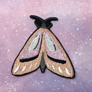 K&ouml;nnte beinhalten: Ein gestickter Motten-Patch in Rosa und Braun mit schwarzen Akzenten. Die Motte hat eine Fl&uuml;gelspannweite von etwa 5 cm.