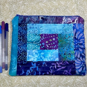 May include: A blue and purple patchwork zippered pouch with a quilted design. The pouch is made of fabric with a batik pattern.