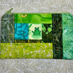 May include: A green quilted zippered pouch with a frog design. The pouch is made of fabric with a green and brown batik pattern.
